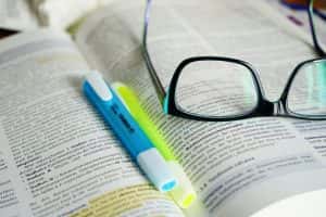 Pair of spectacles and highlighter pens sitting on an open textbook