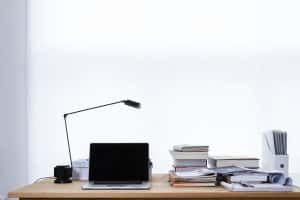 Laptop and piles of books with reading lamp on desk