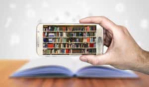 Hand holding a smart phone displaying shelves of books in front of an open book